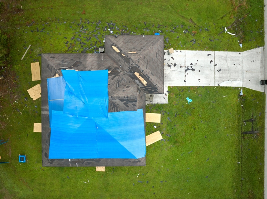 Aerial view of damaged in hurricane Ian house roof covered with blue protective tarp