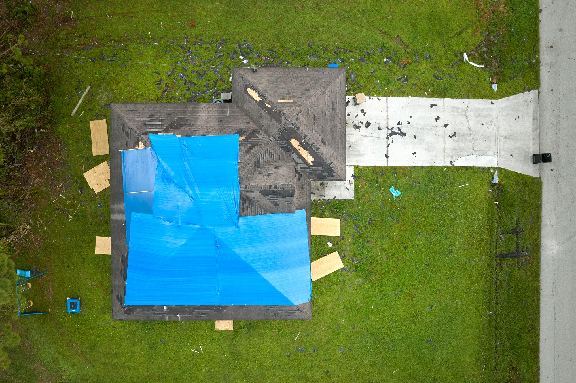 Aerial view of damaged in hurricane Ian house roof covered with blue protective tarp